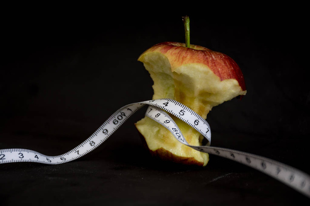 Apple söi mittarin ympäri mustalla taustalla ilmaisee käsitteen anoreksia
 - Valokuva, kuva
