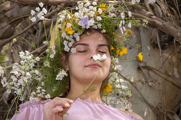 Портрет усміхненої молодої жінки в вінку з квітами, що нюхає квітку крупним планом
 - Фото, зображення