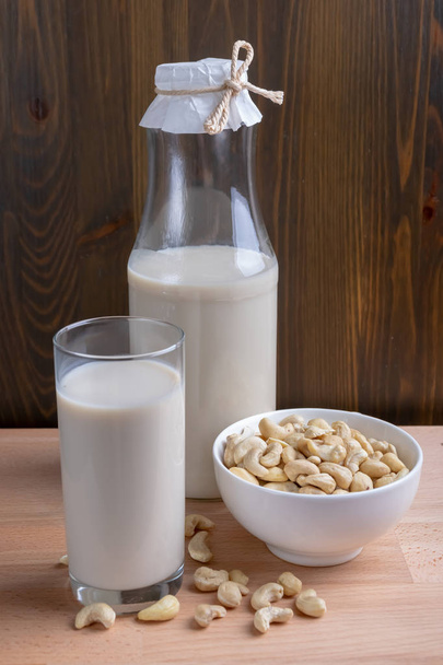 Кешью молоко из стекла и органического кешью на деревянном фоне, альтернативное молоко
 - Фото, изображение