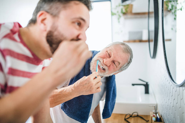 An adult hipster son and senior father brushing teeth indoors at home. - Photo, Image