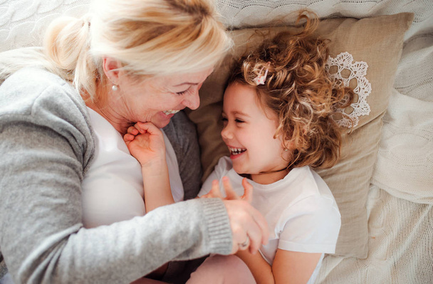 A top view portrait of small girl with grandmother having fun at home. - Photo, Image