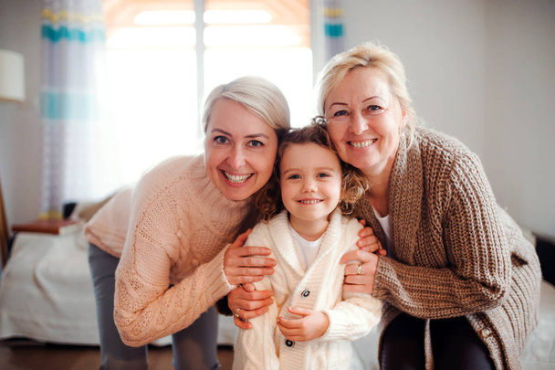A portrait of small girl with mother and grandmother at home. - Foto, afbeelding