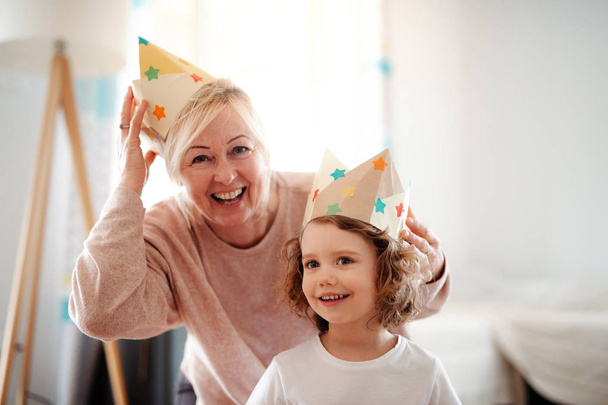 A portrait of small girl with grandmother at home, having fun. - Foto, afbeelding