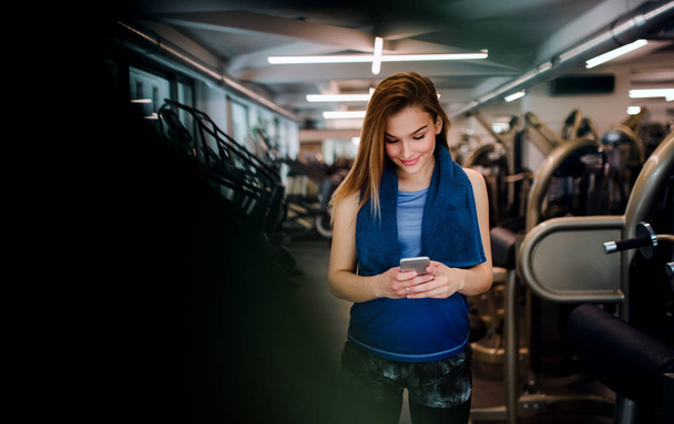 A portrait of young girl or woman with smartphone in a gym. - Фото, зображення