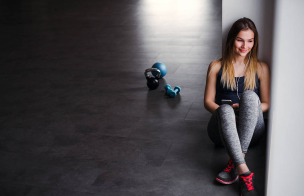 A young girl or woman with earphones and smartphone in a gym. - Foto, Imagem