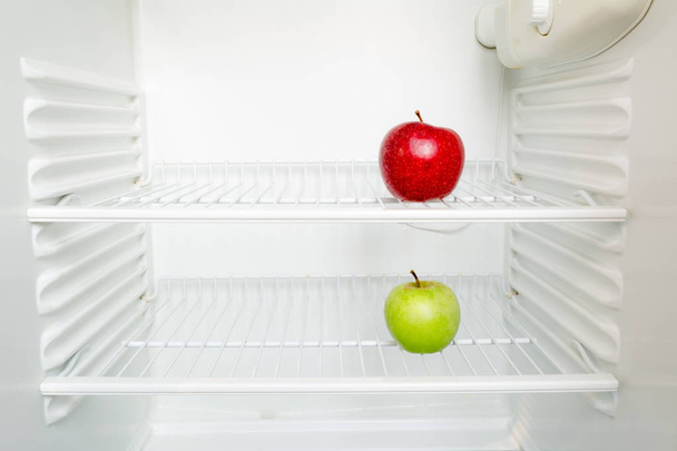Bright fresh red and green apples on shelf of open empty refrigerator. Weight loss diet concept. - Fotó, kép