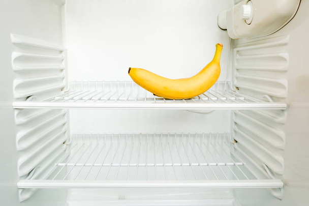 Bright fresh banana on shelf of open empty refrigerator. Weight loss diet concept. - Foto, imagen