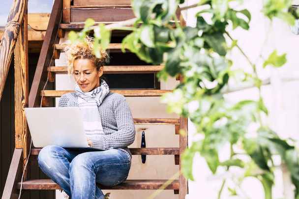 Krásná středního věku mladá běloška pracující na notebooku počítač internet připojený outdor domácí sednout na dřevěné schodiště - pěkný životní styl pro podnikání - Fotografie, Obrázek