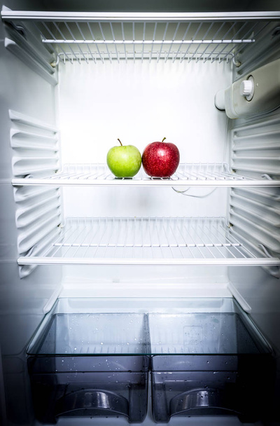 Bright fresh red and green apples on shelf of open empty refrigerator. Weight loss diet concept. - Foto, Imagen