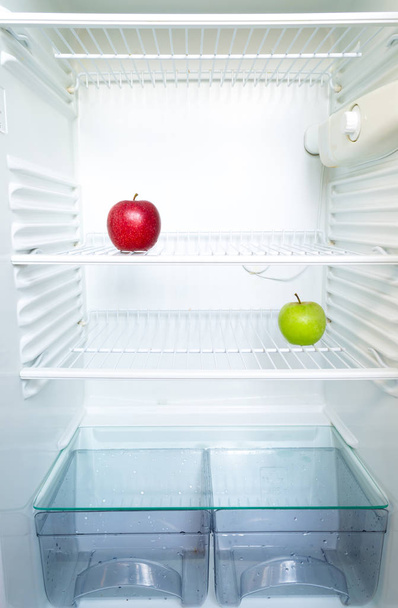 Bright fresh red and green apples on shelf of open empty refrigerator. Weight loss diet concept. - Фото, изображение