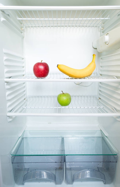 Élénk friss piros és zöld alma és banán a polcról a nyitott üres hűtőszekrény. Fogyás diéta koncepció. - Fotó, kép
