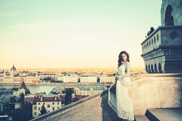 Girl with glamour look. Woman in white wedding dress on city view, fashion. Sensual woman with long hair on balcony, beauty. Bride with makeup. Fashion model style and hairstyle - Zdjęcie, obraz