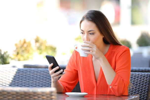 Egy nő kávét iszik, okos telefont néz egy bárban. - Fotó, kép