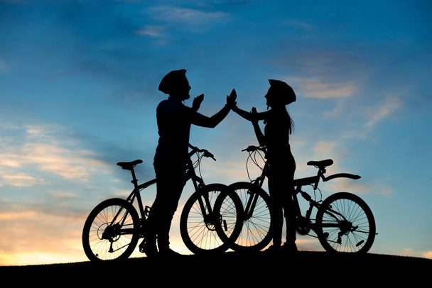 Cheerful couple of bicyclists clapping hands at sunset. - Фото, зображення