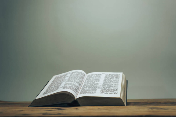 Abra la Sagrada Biblia sobre una antigua mesa de madera de roble. Fondo de pared gris. - Foto, Imagen