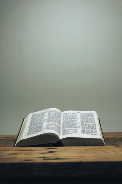 Otwórz Biblię na starym dębowym drewnianym stole. Szare tło ściany. - Zdjęcie, obraz