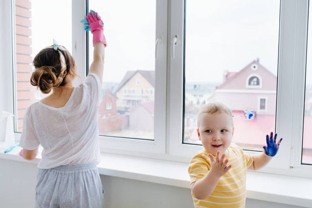 Mother of a toddler boy is cleaning plastic window door with wet cloth - Zdjęcie, obraz