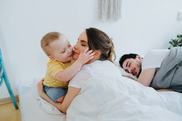 Cute little son trying to wake up his parents. - Zdjęcie, obraz