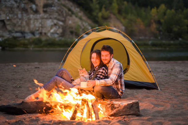 Ihmiset, matkailu ja luonto käsite Mies ja nainen kissansa istua lähellä tulta
 - Valokuva, kuva