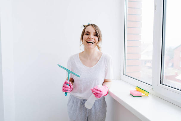 Young brunette woman in pink rubber gloves with window scrubber in hand - Фото, зображення
