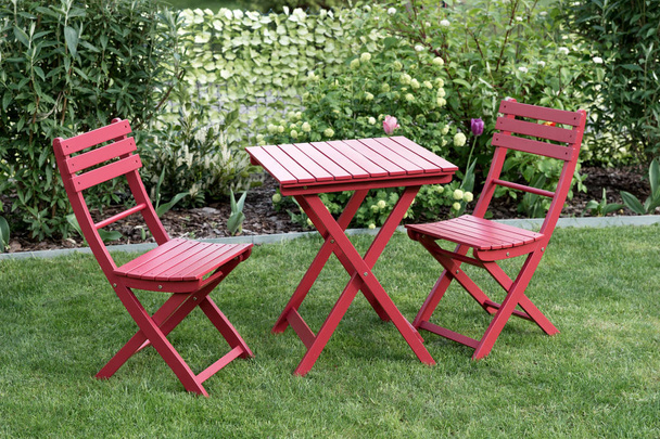 Розслаблююча зона з двома червоними стільцями та червоним столом у затишному саду
 - Фото, зображення