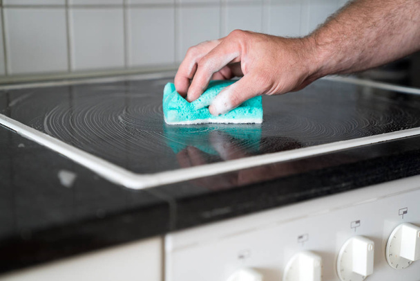 modern house husband cleaning a stove in the kitchen with a spon - Foto, imagen