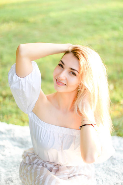 Портрет молодой блондинки, улыбающейся девушке, сидящей на клетке, трава на заднем плане
. - Фото, изображение