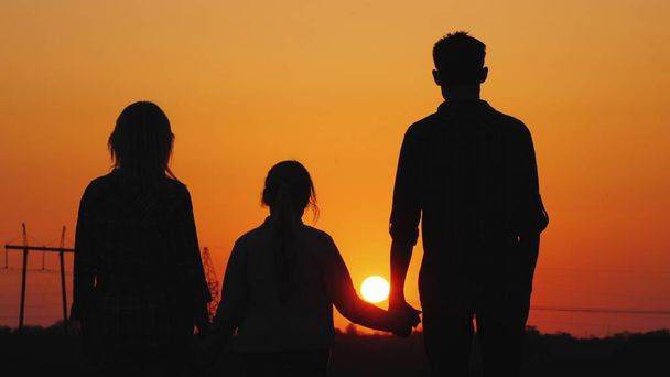Rodina tří obdivuje oranžový západ slunce nad městem, zadní pohled - Fotografie, Obrázek