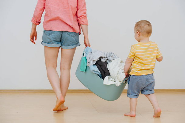 Young mother and her happy toddler son with laundry basin full of washed towels - Fotoğraf, Görsel