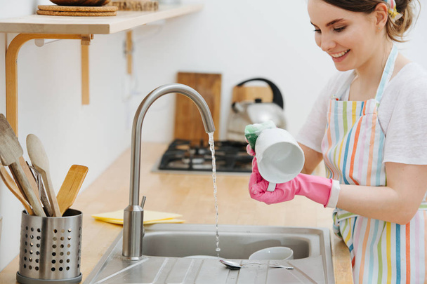 Young happy woman in a kitchen is washing cups and dishes - Foto, Imagen