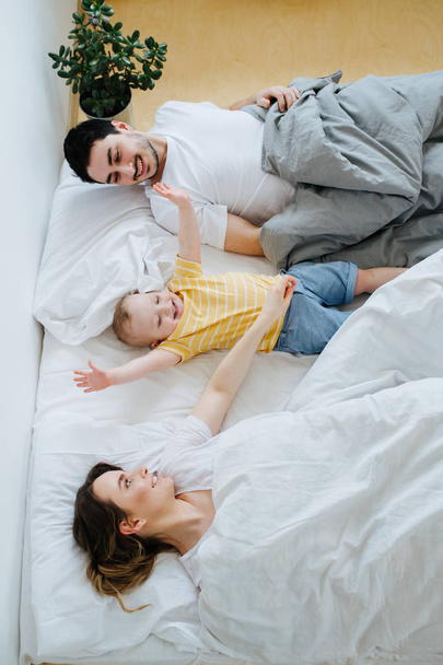 Young family resting together in parent's bed in the morning - Valokuva, kuva