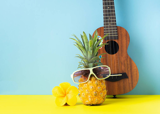 Yellow ripe pineapple in sunglasses. Guitar on yellow blue background. Funny muzzle of a tropical fruit. Party concept. - Foto, afbeelding
