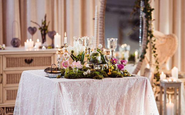 A table for two. Romantic atmosphere in subdued light, lighted candles and rustic decoration (forest moss, flowers, glasses and vases) - Photo, Image