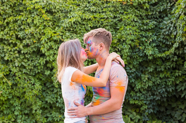 Holiday, holi and people concept - Happy couple having fun with multicolored powder on their faces - Photo, Image