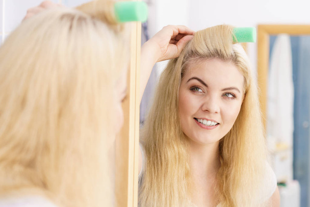 Blonde woman using hair rollers - Foto, afbeelding