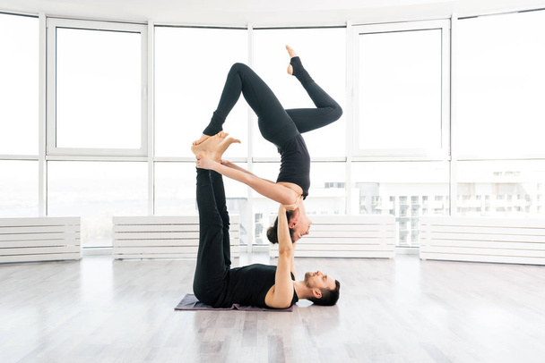 Положительная женщина практикует акро йогу с мужчиной партнером в студии
 - Фото, изображение