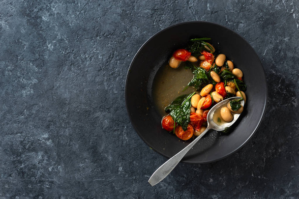 Dinner bowl of stewed white beans with vegetables on a dark background top view - Foto, Bild