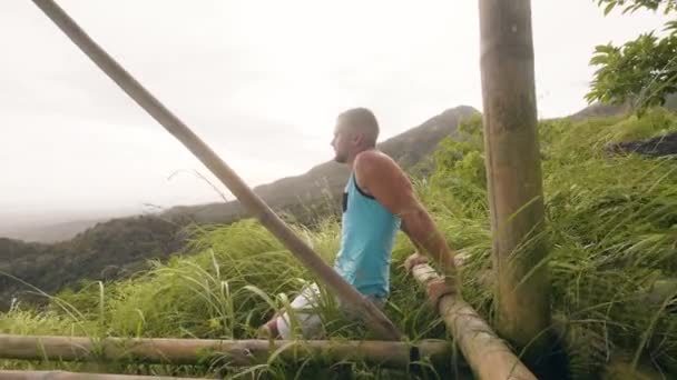Jóképű ember csinál push up gyakorolni a zöld dombon és trópusi hegyvidéki táj. Testépítő képzés tolja fel karját izmok trópusi táj. Szabadtéri férfi edzés. - Felvétel, videó