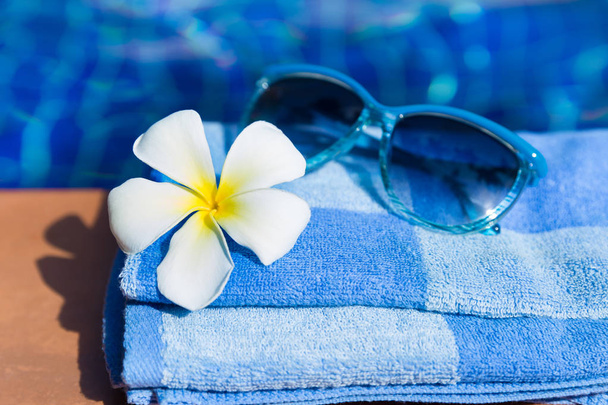 Fluffy towel with sunglasses and flower on border of a swimming pool - Photo, image