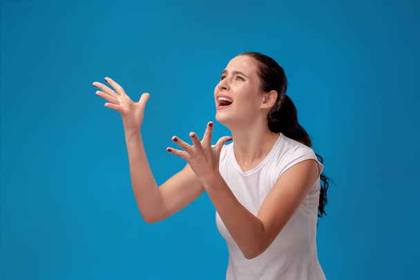 Portrait studio d'une jeune belle femme en t-shirt blanc sur fond de mur bleu. Les gens émotions sincères
. - Photo, image