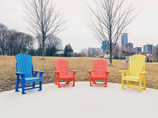 Neljä värikästä punaista, sinistä ja keltaista puista muskokaa Adirondack-tuolia seisomassa rivissä puistossa kevään syyspäivänä. Käsitteen rentoutumista ja rauhallinen puhua keskustelua ystävien tai perheen
. - Valokuva, kuva