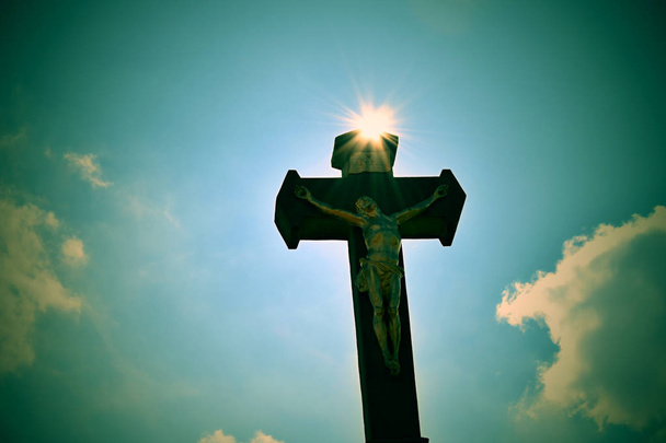 Křesťanský kříž proti modrému nebi. Kamenný křesťanský kříž na modré obloze s mraky a slunečními paprsky - Fotografie, Obrázek