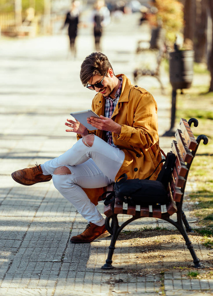 Курящий бизнесмен в желтом пальто, расслабляющийся в городском парке
 - Фото, изображение