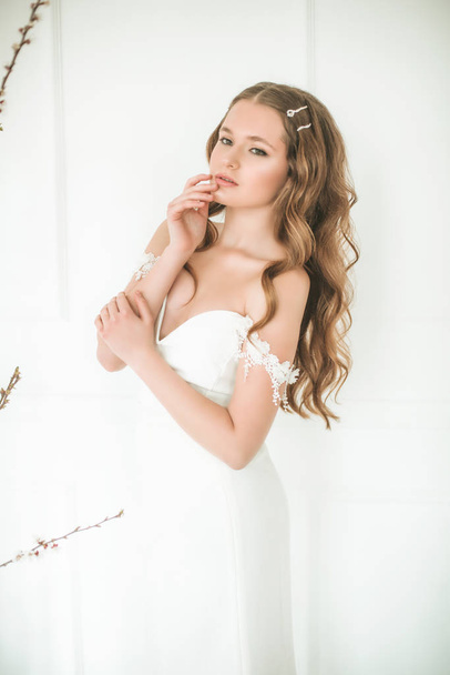 Beautiful young bride in a white dress with beautiful decorations in a bright studio - Photo, image