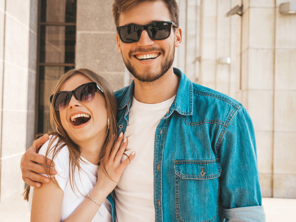 Smiling beautiful girl and her handsome boyfriend in casual summer clothes. Happy cheerful family having fun on the street background in sunglasses - Foto, afbeelding