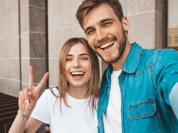 Smiling beautiful girl and her handsome boyfriend in casual summer clothes. Happy family taking selfie self portrait of themselves on smartphone camera. Having fun on the street background  - 写真・画像