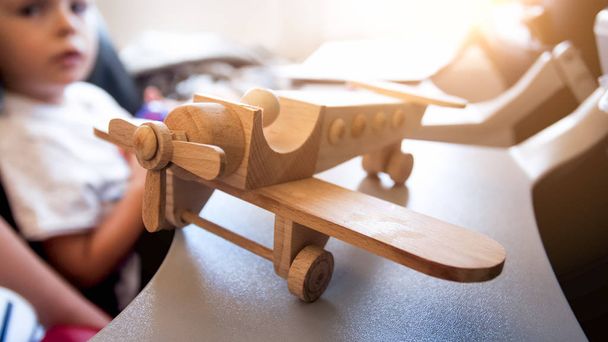 Closeup image of wooden airplane miniature against little boy sitting in passenger seat during flight - Zdjęcie, obraz
