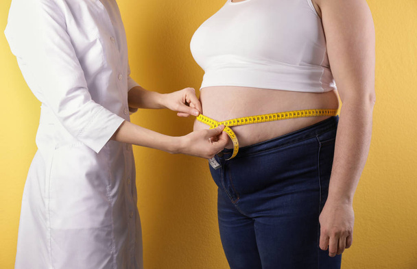 Doctor measuring waist of overweight woman on color background, closeup - Photo, Image