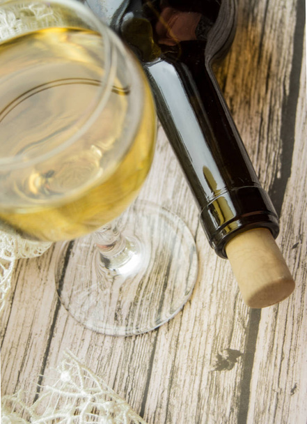 Una copa de vino blanco y una botella sobre una mesa de madera. Vista superior, plano vertical, plano
 - Foto, imagen