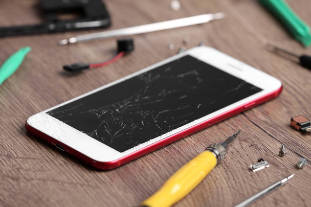 Modern phone with broken display and repair tools on table - 写真・画像